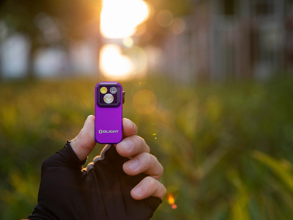 Latarka OLIGHT OL691572, szybkie ładowanie, USB-C, akumulator, gotowość, Fioletowa Oclip Pro trzymana w rękawiczce, zachód słońca i zielone tło, sportowa elegancja.