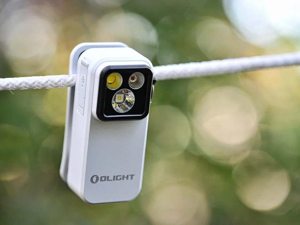 Latarka OLIGHT OL692753, trzy tryby, wszechstronna, lekka, do awaryjnych, Oclip Pro biały przypięta do sznurka, rozmyte zielono-żółte tło, wyrazisty klips.
