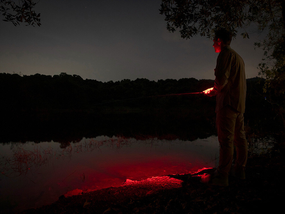Latarka OLIGHT OL692753, aluminium, odporność, IPX6, outdoor, Wędkarz oświetla brzeg czerwonym światłem Oclip Pro podczas nocnej zasiadki nad wodą.