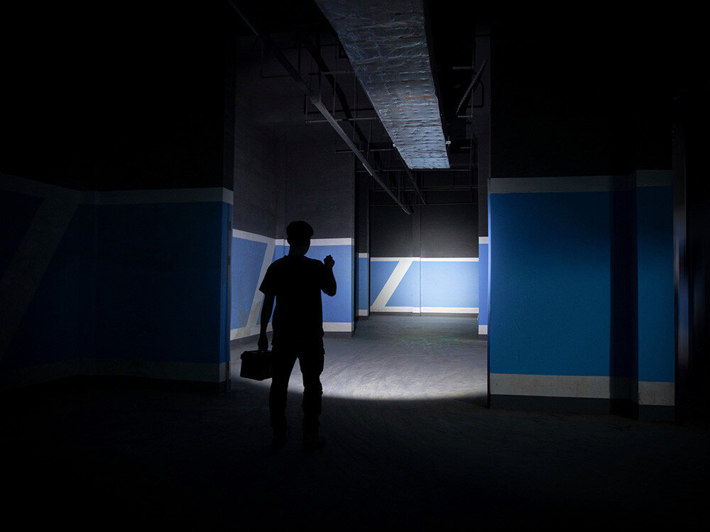 Latarka OLIGHT OL693934, długie działanie, tryby, widoczność, regulacja, Silna wiązka światła Olight Oclip Pro, pracownik oświetla wnętrze hali, niebieskie ściany.