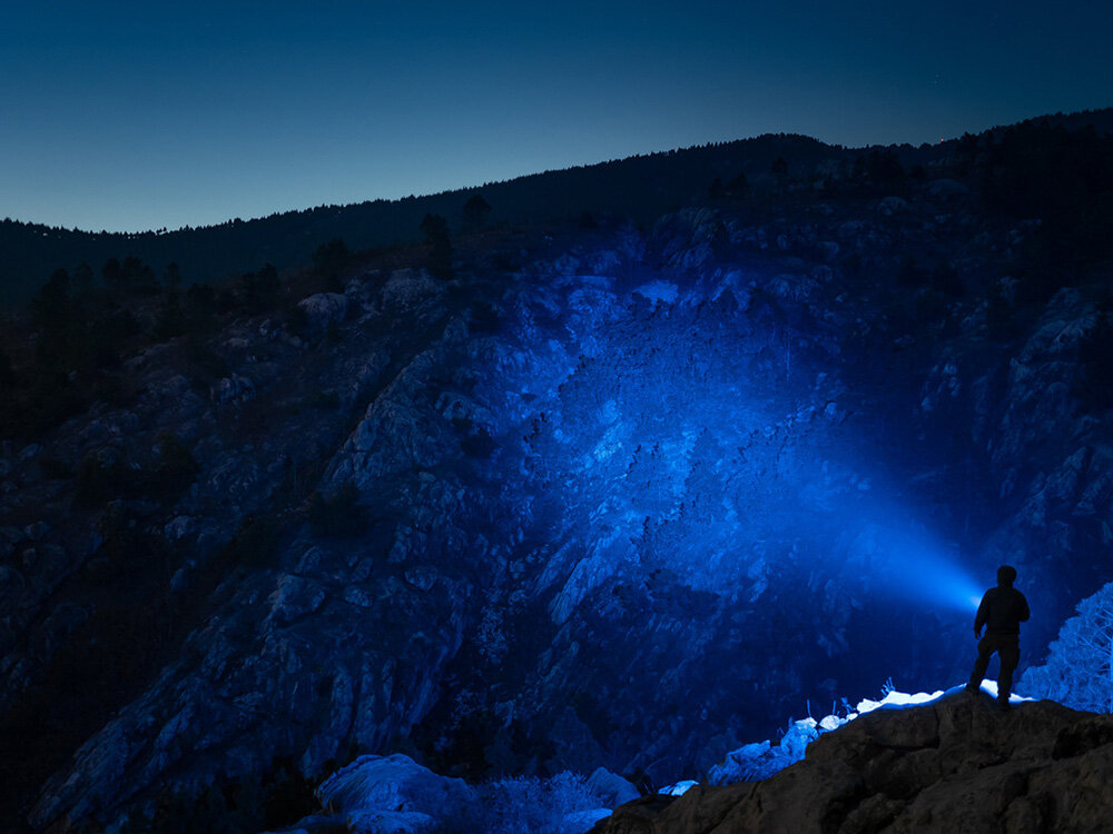 Latarka OLIGHT Marauder Mini QL000549 Niebieski, przycisk, rotacja, LED, blokada, Niebieska wiązka Marauder Mini rozświetla zbocze skalne, góry w nocy, postać z latarką.