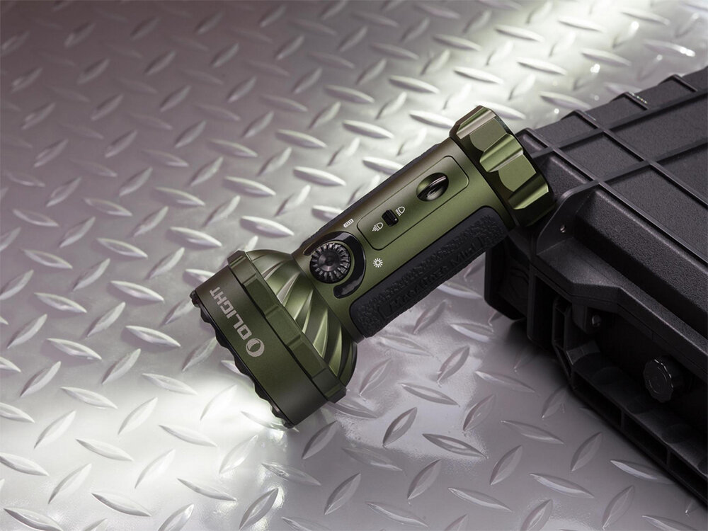 Latarka OLIGHT Marauder Mini QL000983 Zielony, akumulator, ładowanie, wskaźnik, MCC3, Olight Marauder Mini w kolorze zielonym, świeci pod kątem, na metalowej powierzchni, oparta o czarną walizkę.