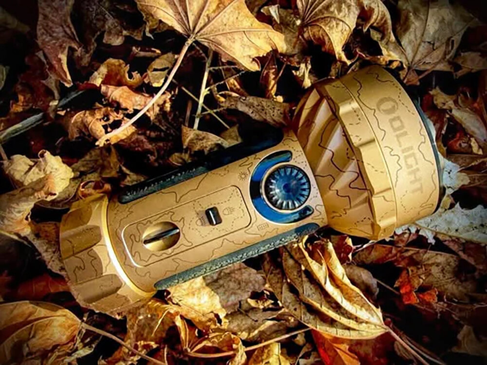 Latarka OLIGHT Marauder Mini QL691626 Piaskowy, akumulator, ładowanie, wskaźnik, MCC3, Latarka Olight Marauder Mini Desert leży wśród suchych liści, teren outdoorowy, matowy wzór.