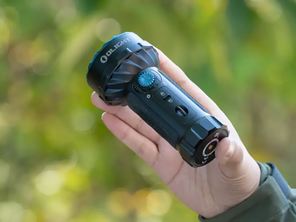 Latarka OLIGHT Marauder Mini QL000495 Czarny, akumulator, ładowanie, wskaźnik, MCC3, Marauder Mini trzymana w dłoni, ergonomiczny kształt i niebieski przycisk, zielone tło.