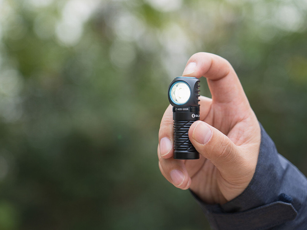 Latarka czołowa OLIGHT Perun 2 Mini QL000648, latarka, mini, światło, zasięg, Dłoń trzyma ergonomiczną latarkę Olight, jasne światło w plenerze, zielone tło w rozmyciu.