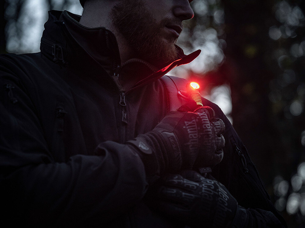 Latarka czołowa OLIGHT Perun 2 Mini QL000648, opaska, silikon, czołówka, kątowa, Mężczyzna w rękawicach taktycznych przypina czerwone światło Olight do klapy kurtki po zmroku.