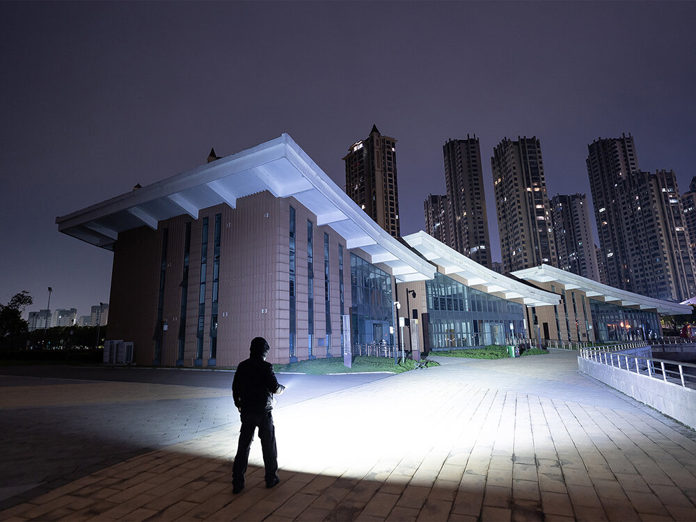 Latarka OLIGHT Prowess QL690681, moc, lumeny, wyjątkowe, światło, Osoba z latarką Olight Prowess świeci w stronę futurystycznego budynku nocą.