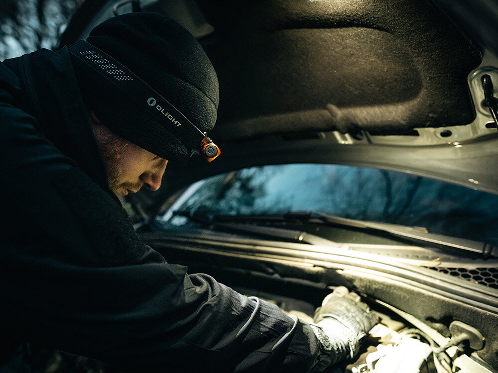 Latarka czołowa OLIGHT QL000594, ergonomia, moc, zasilanie, światło, Mechanik w czapce Olight naprawia auto wieczorem, jasna czołówka oświetla komorę silnika.