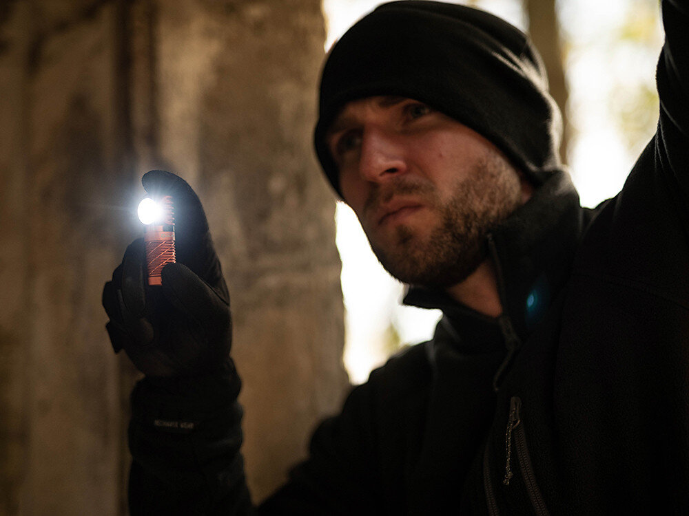 Latarka czołowa OLIGHT QL000594, latarka, mini, światło, zasięg, Dłoń trzyma ergonomiczną latarkę Olight, jasne światło w plenerze, zielone tło w rozmyciu.