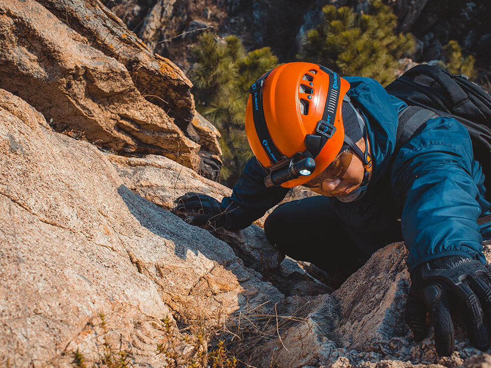 Latarka czołowa OLIGHT Perun 2 QL005063, światło, latarka, oświetlenie, praca, Pracownik z czerwoną kaskiem oświetla pusty, surowy garaż latarką, jasne, rozproszone światło.