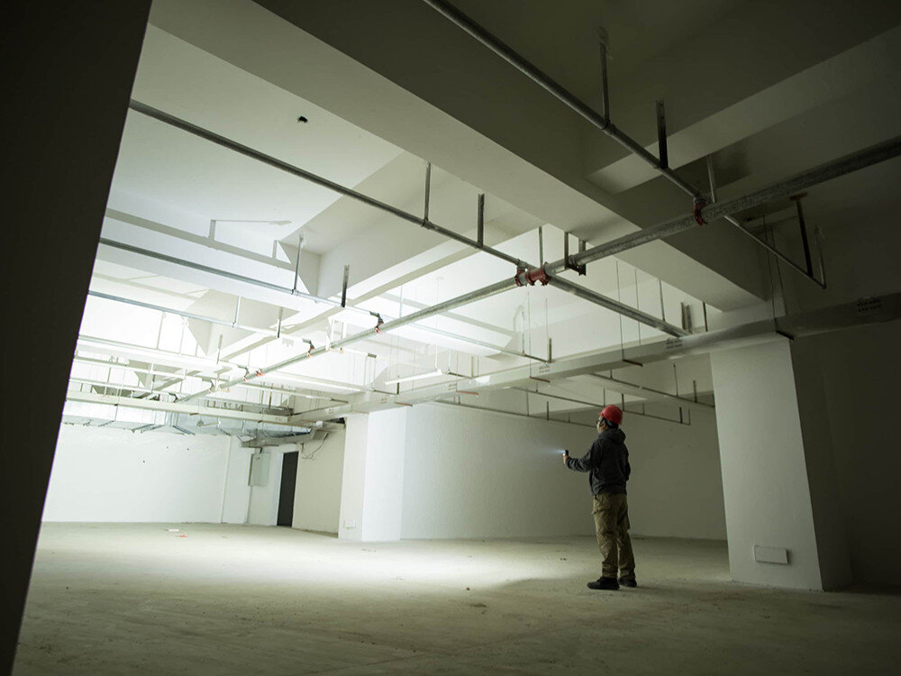 Latarka czołowa OLIGHT Perun 2 QL005063, akumulator, ładowanie, magnetyczne, MCC3, Pracownik z czerwoną kaskiem oświetla pusty, surowy garaż latarką, jasne, rozproszone światło.