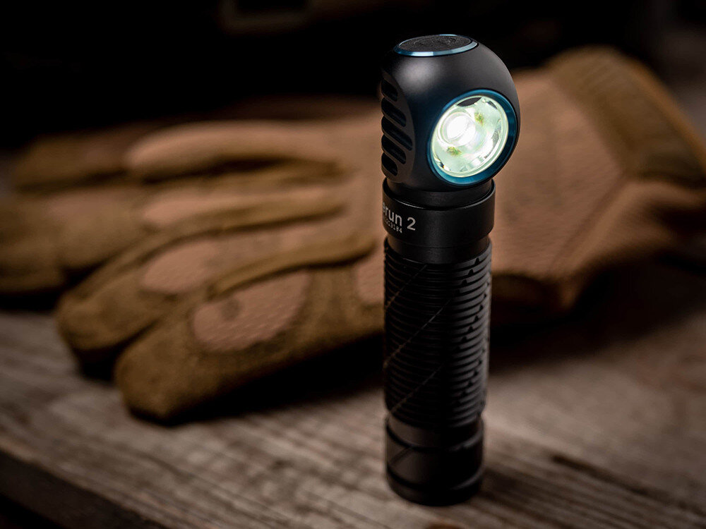 Latarka czołowa OLIGHT Perun 2 QL121745, aluminium, anodyzacja, IPX8, ochrona, Latarka Olight na stole z rękawicami, stojąca pionowo, świeci białym światłem, warsztat.