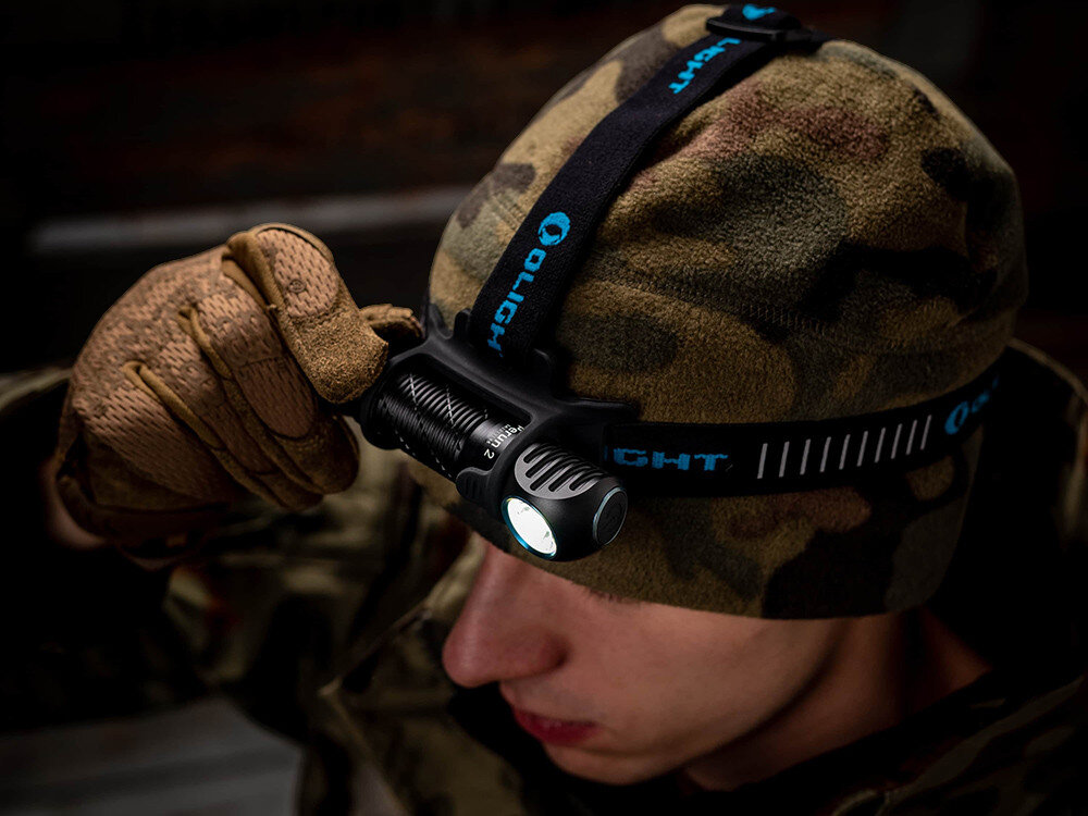 Latarka czołowa OLIGHT Perun 2 QL121745, tryby, SOS, jasność, czas, Człowiek w rękawicach i czapce w moro poprawia czołówkę Olight, jasne światło, ciemne tło.