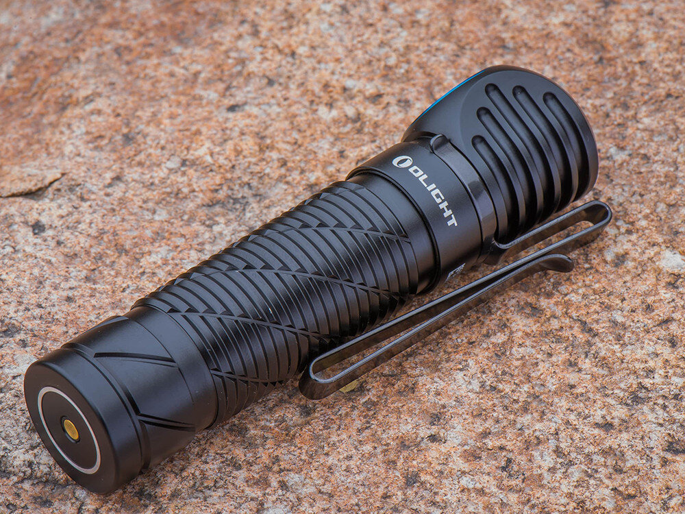 Latarka czołowa OLIGHT Perun 2 QL121745, magnes, klips, montaż, kieszeń, Latarka Olight leży na kamiennym podłożu, czarna obudowa, duży klips, teksturowany korpus.