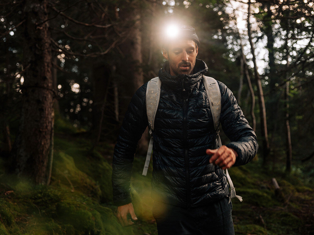 Latarka czołowa OLIGHT Perun 3 QL690193, latarka, Perun 3, moc, zasięg, Turysta w lesie, latarka przymocowana na głowie, jasne światło oświetla ścieżkę, kurtka puchowa.