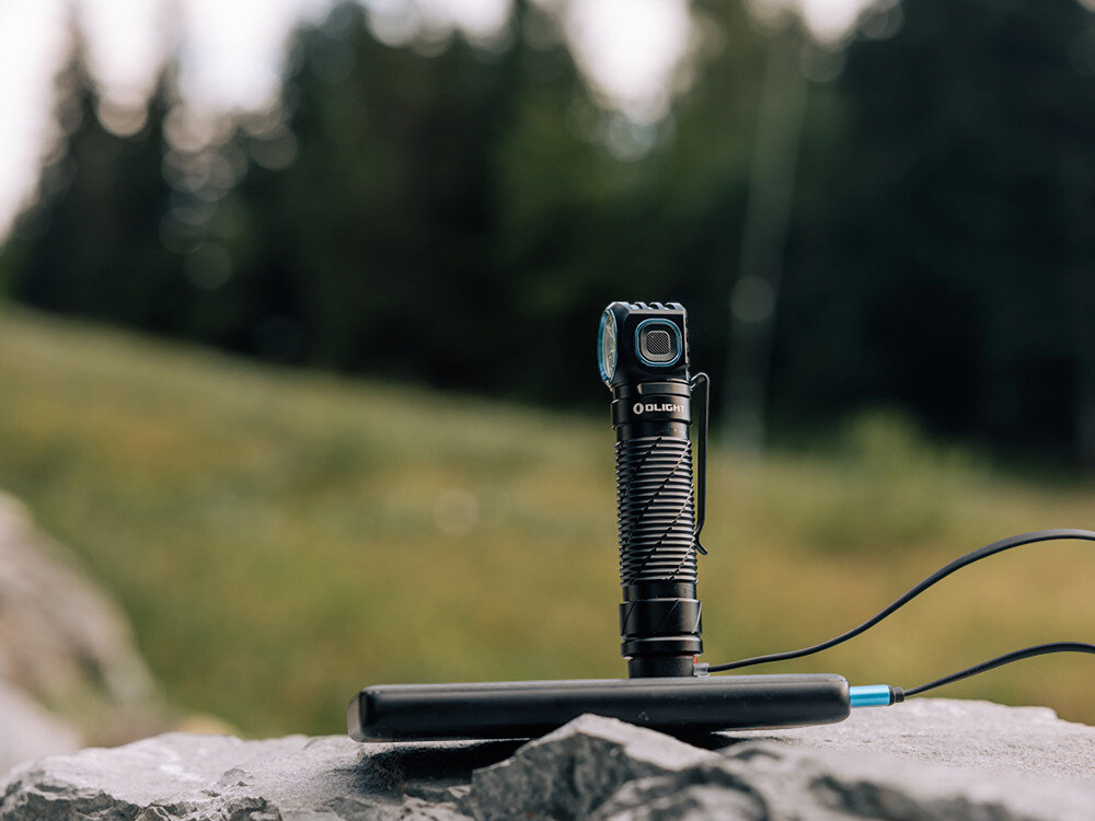 Latarka czołowa OLIGHT Perun 3 QL690193, akumulator, 21700, ładowanie, magnetyczne, Latarka Olight ładowana powerbankiem na kamieniu, przewód USB, plener, rozmyte tło.