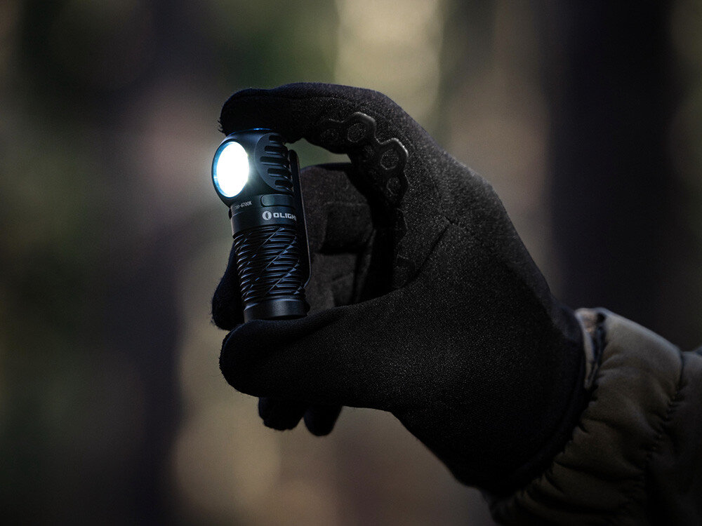 Latarka czołowa OLIGHT Perun 3 Mini CW QL690759, akumulator, magnetyczna, ładowarka, wskaźnik, Czarna latarka Olight w czarnej rękawiczce oświetla otoczenie, wysokie kontrasty, ciemny las.
