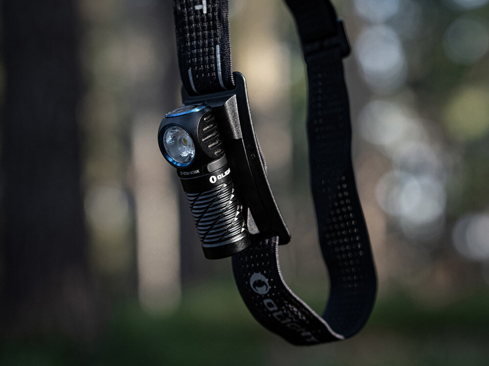 Latarka czołowa OLIGHT Perun 3 Mini CW QL690759, opaska, regulacja, odblask, komfort, Latarka Olight umieszczona na opasce wiszącej na tle rozmytego lasu, detale produktu.