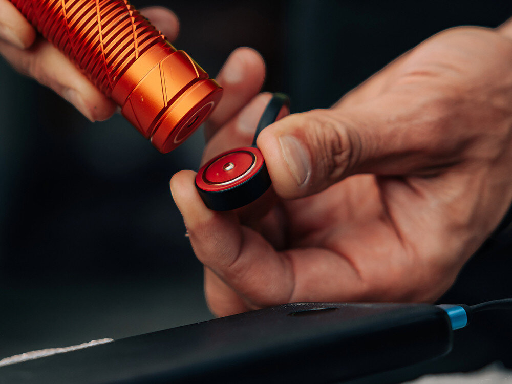 Latarka czołowa OLIGHT Perun 3 QL690216, akumulator, 21700, ładowanie, magnetyczne, Zbliżenie na przypięcie i ładowanie latarki Olight, ręka trzyma złącze magnetyczne, oryginalna ładowarka.