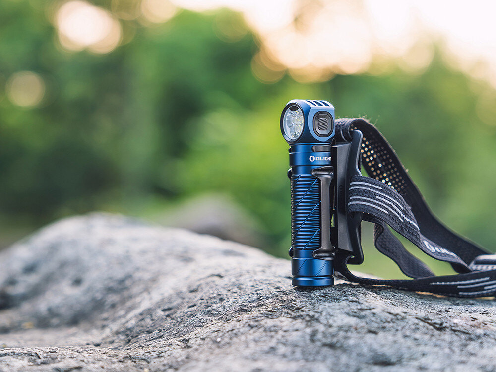 Latarka czołowa OLIGHT Perun 3 QL690490, LED, czołówka, 3000 lumenów, ergonomia, Latarka Olight Perun 3 na pasku nagłownym, leży na skale, zielone rozmyte tło liści.