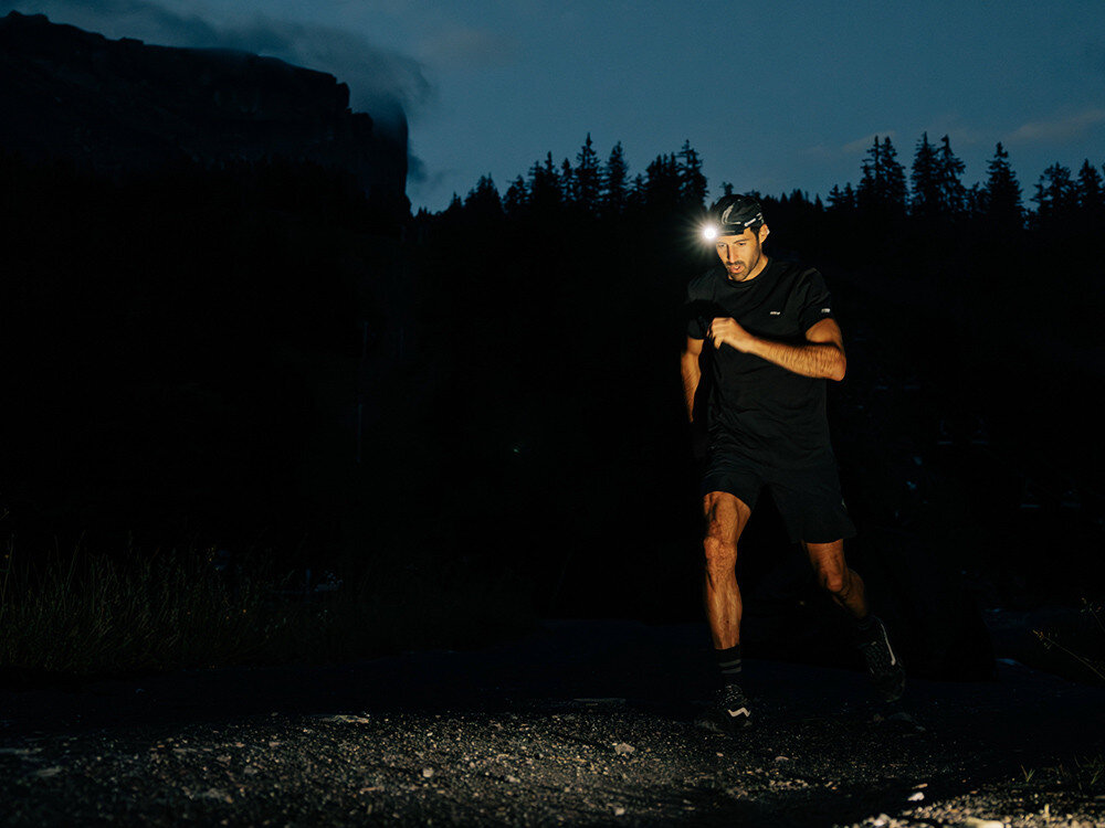 Latarka czołowa OLIGHT Perun 3 QL691534, czujnik, jasność, stabilizacja, wibracje, Biegacz nocą na górskim szlaku, mocna czołówka podkreśla teren, dynamiczna sylwetka.