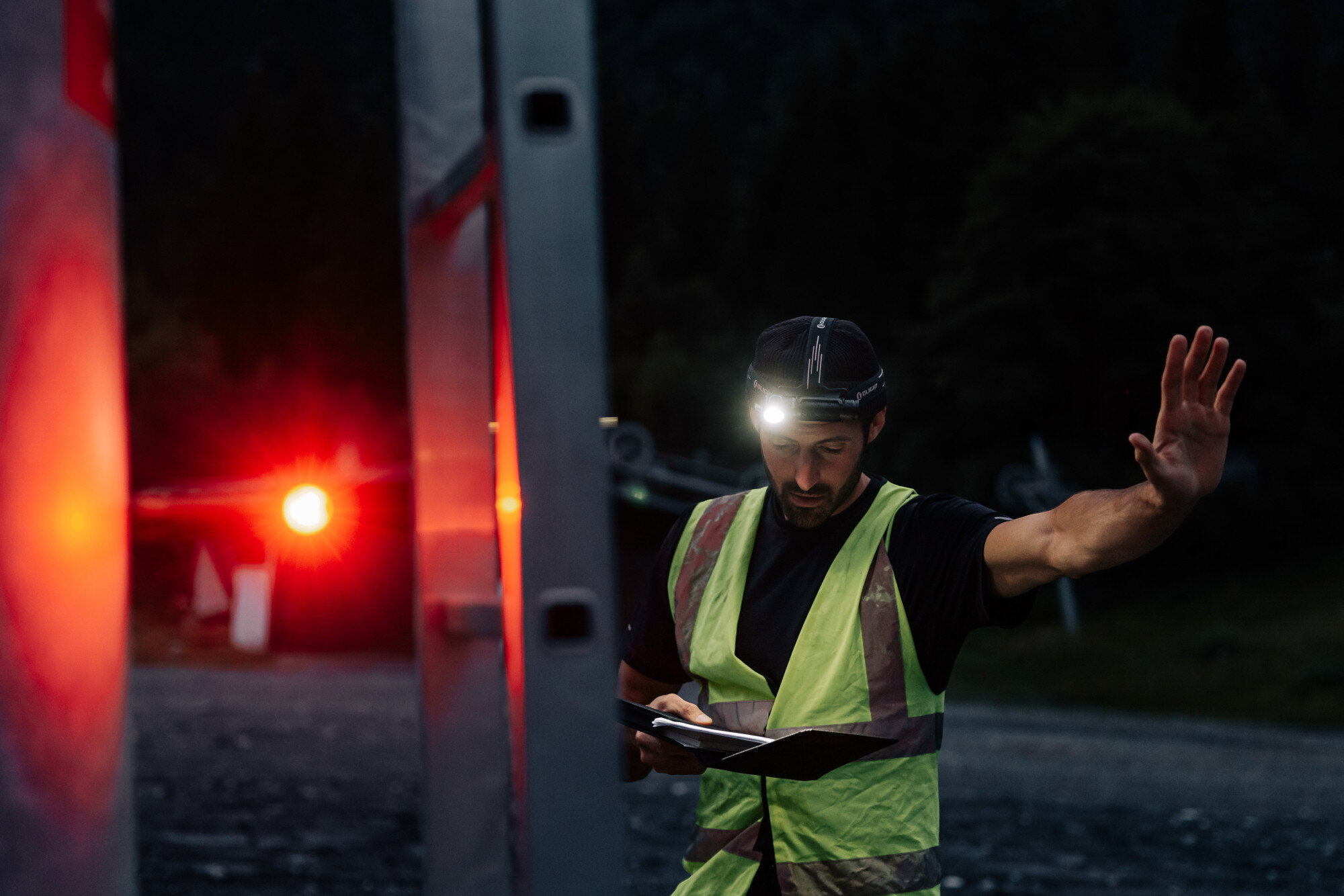 Latarka czołowa OLIGHT Perun 3 QL691534, opaska, klips, magnes, montaż, Pracownik w kamizelce odblaskowej, czołówka Olight na głowie, nocna praca, czerwone światło w tle.