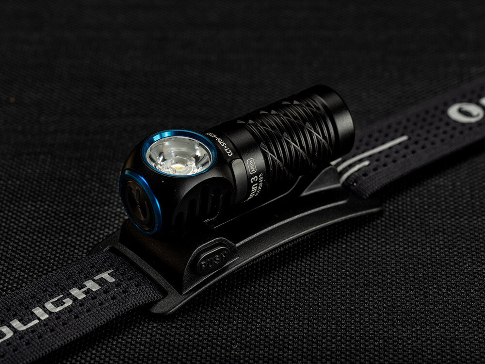 Latarka czołowa OLIGHT Perun 3 Mini QL692401, mini, jasność, diody, zasięg, Czarna latarka Olight w uchwycie na opasce, szczegółowo pokazana soczewka, tło czarne.