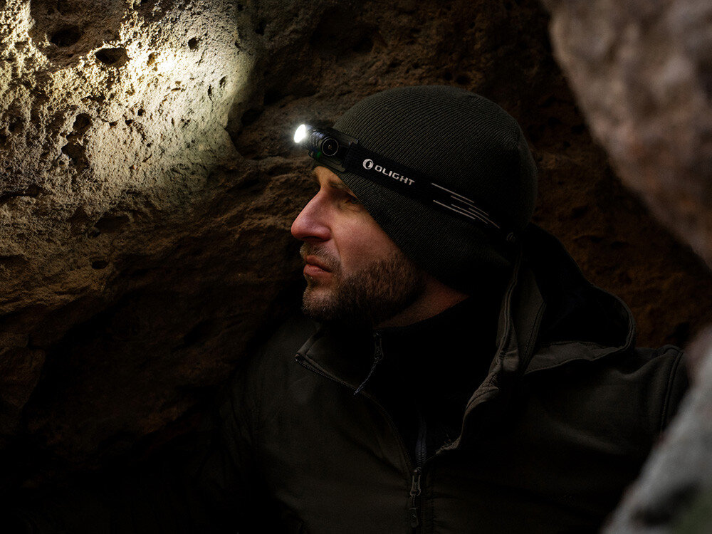 Latarka czołowa OLIGHT Perun 3 Mini Premium QL691282, światło, oświetlenie, ergonomia, uniwersalność, Osoba w czapce z latarką czołową Olight, oświetlająca skały podczas eksploracji.