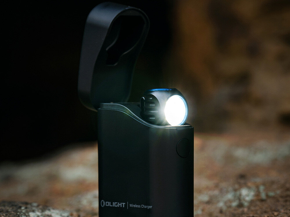 Latarka czołowa OLIGHT Perun 3 Mini Premium QL691282, system, zabezpieczenia, diody, przycisk, Latarka Olight w etui ładującym, oświetlająca ciemne tło skalne w plenerze.