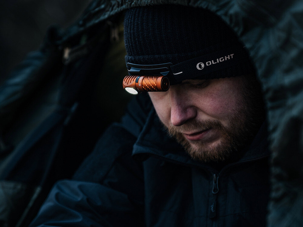 Latarka czołowa OLIGHT Perun 3 Mini QL692418, moc, światło, ergonomia, oświetlenie, Mężczyzna w czapce Olight, z pomarańczową czołówką, skryty pod płachtą, wieczorna wyprawa.