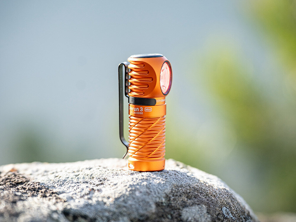 Latarka czołowa OLIGHT Perun 3 Mini QL692418, mini, jasność, diody, zasięg, Pomarańczowa Olight Perun 3 Mini pionowo na skale, ujęcie w słońcu, wyraziste żłobienia korpusu.