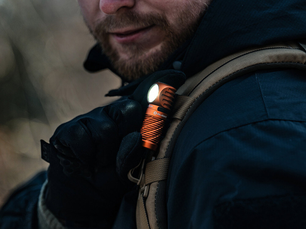 Latarka czołowa OLIGHT Perun 3 Mini QL692418, magnes, podstawa, klips, smycz, Mężczyzna w rękawiczkach przypina świecącą latarkę Olight do szelki plecaka, uśmiech, outdoor.