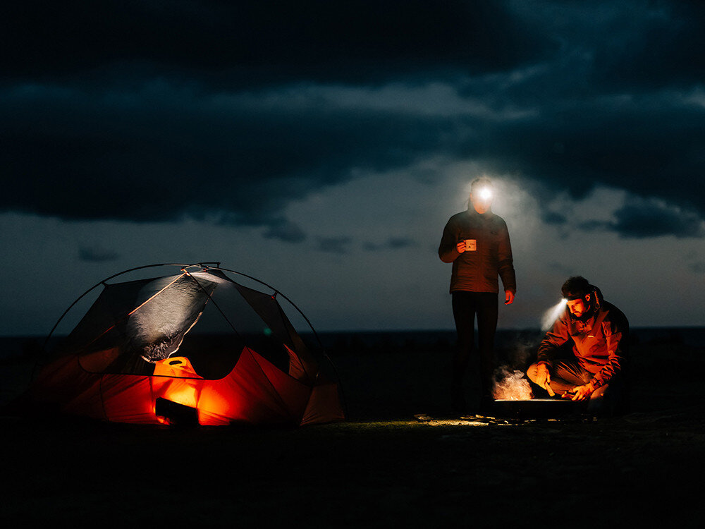 Latarka czołowa OLIGHT Array 2 Pro QL007913, światło, podążanie, oświetlenie, latarka, Biwak nocą, dwie osoby z latarkami Olight, namiot podświetlony, ognisko, krajobraz po zmroku.