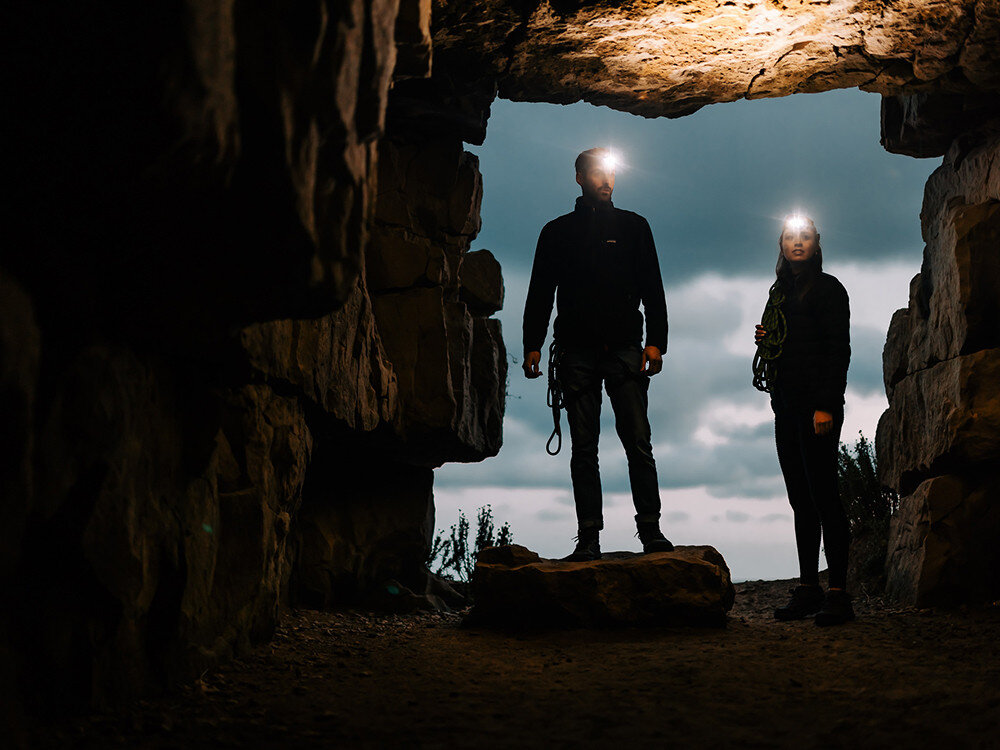 Latarka czołowa OLIGHT Array 2 Pro QL007913, elektronika, stabilizacja, żywotność, solidność, Dwie osoby w grocie z latarkami Olight, silne światła czołowe, wejście jaskini, sylwetki nocą.