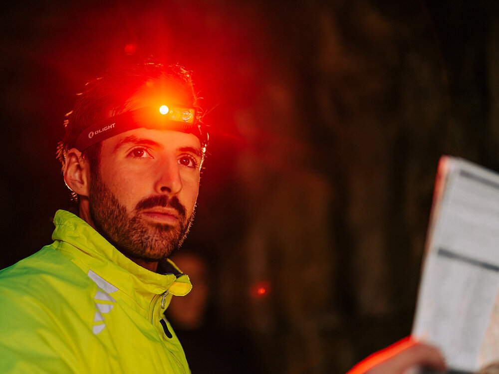 Latarka czołowa OLIGHT Array 2 Pro QL128782, aluminium, IPX4, opaska, diody, Mężczyzna z Olight Array 2 Pro aktywuje tryb czerwonego światła, czyta mapę, wyraźne oświetlenie.