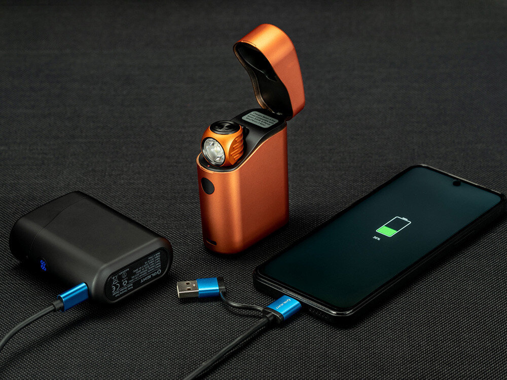 Latarka czołowa OLIGHT Perun 3 Mini Premium QL692395, akumulator, ładowanie, magnetyczne, wskaźnik, Powerbank Olight ładuje telefon, obok etui pomarańczowe z latarką, widok studyjny.