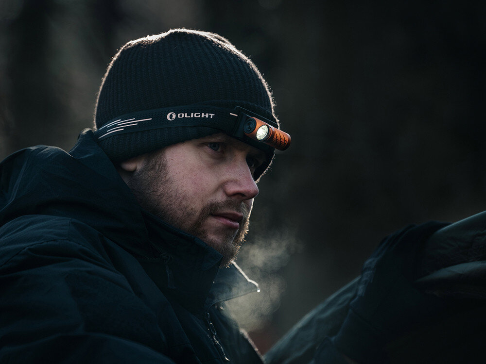 Latarka czołowa OLIGHT Perun 3 Mini Premium QL692395, opaska, regulacja, odblask, komfort, Osoba w czapce z latarką Olight Perun Mini w pomarańczowej wersji, działanie w plenerze.