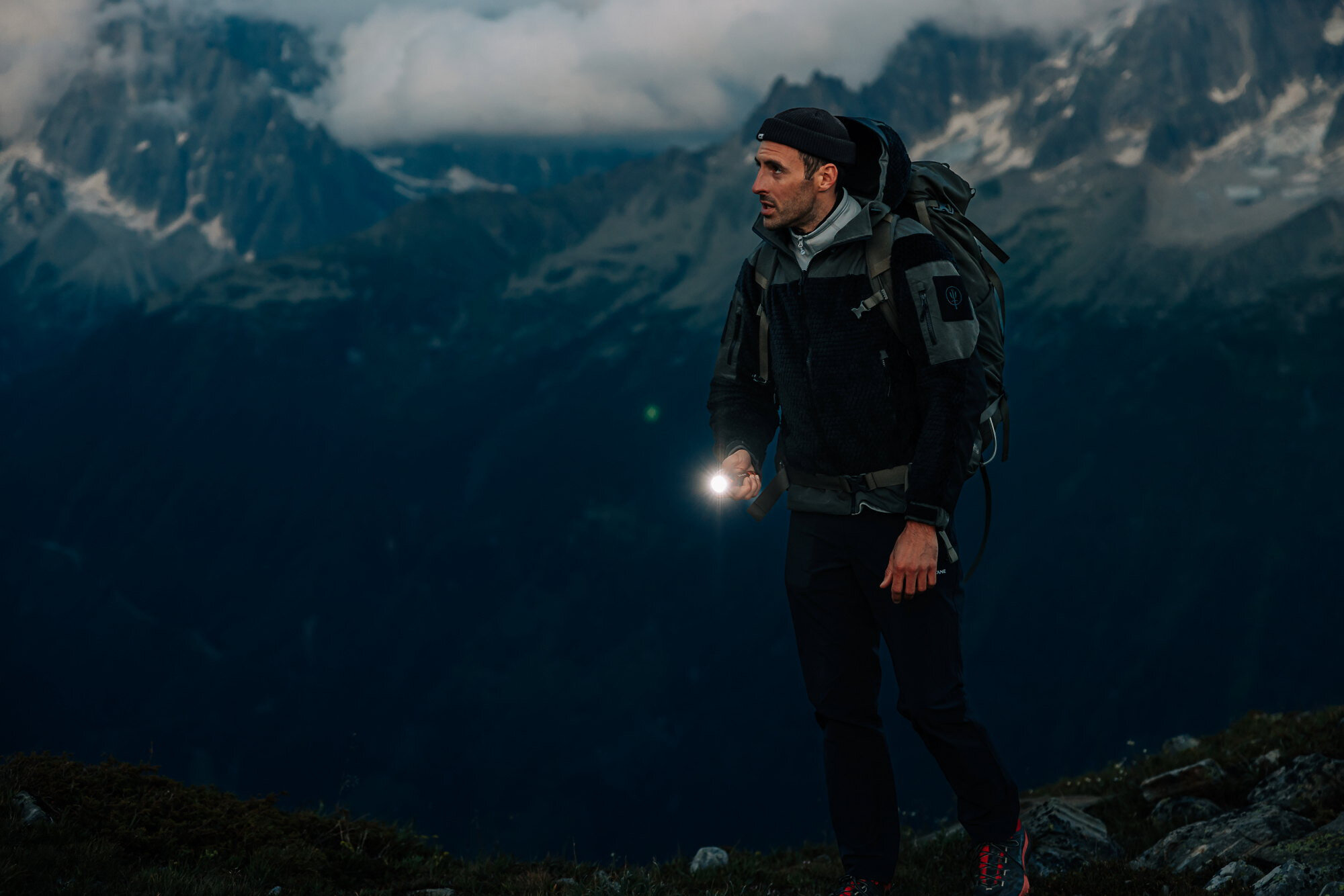 Latarka OLIGHT Seeker 4 Pro OD QL004950, aluminium, obudowa, chwyt, odporność, Mężczyzna podczas trekkingu po zmroku, latarka Olight oświetla kamienisty teren, wysokie góry.