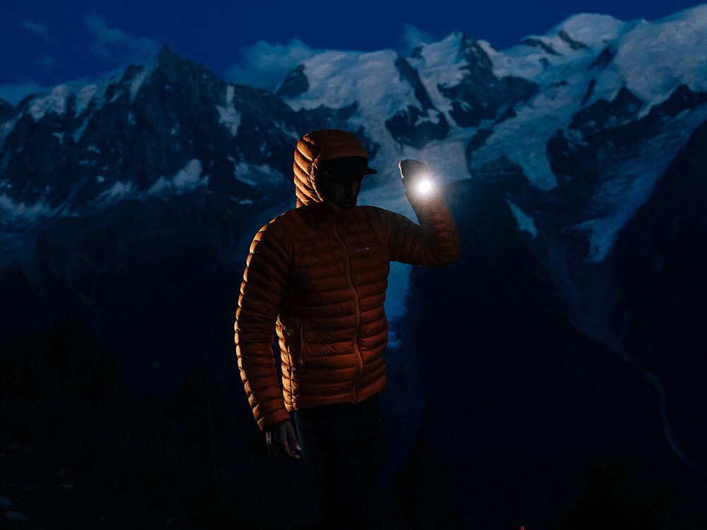 Latarka OLIGHT Seeker 4 Pro QL691022, woda, kurz, szczelność, teren, Postać w kurtce z kapturem, latarka Olight na tle ośnieżonych gór, mocne światło w nocy.