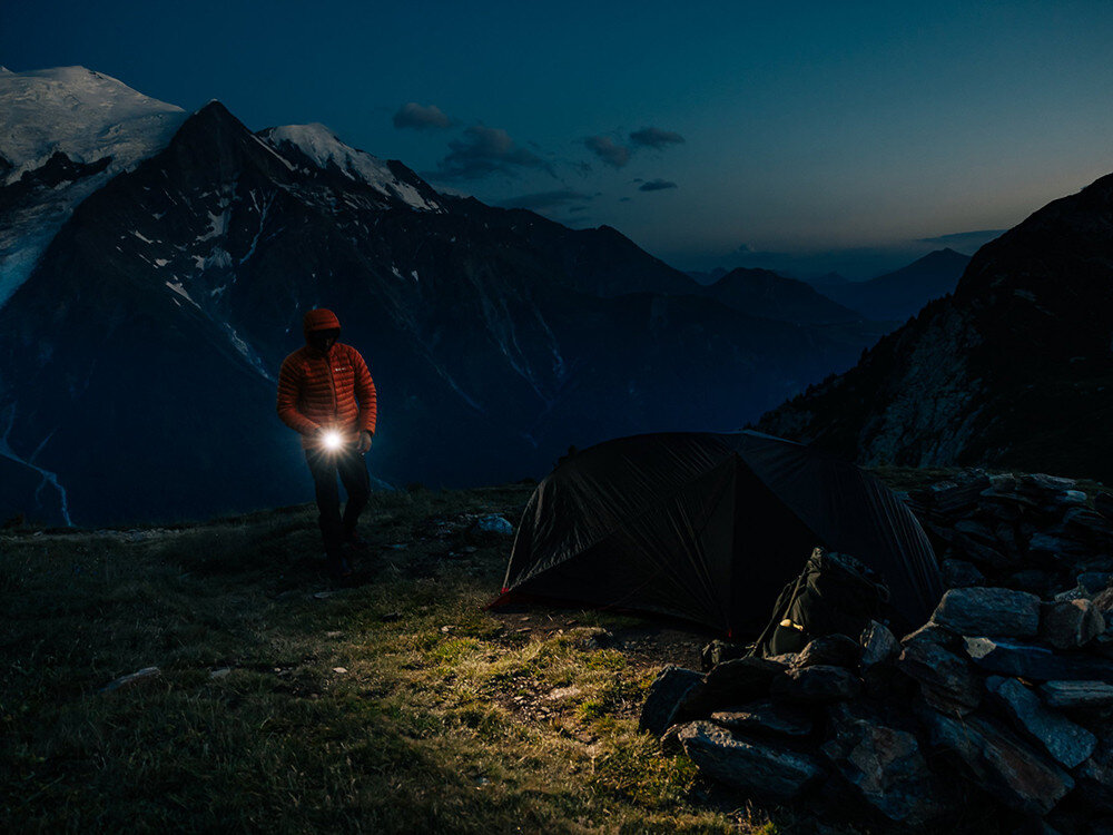 Latarka OLIGHT Seeker 4 Pro QL692197, wydajność, moc, latarka, zasięg, Trekker z latarką Olight przy namiocie o zmierzchu, górski krajobraz z ośnieżonymi szczytami.