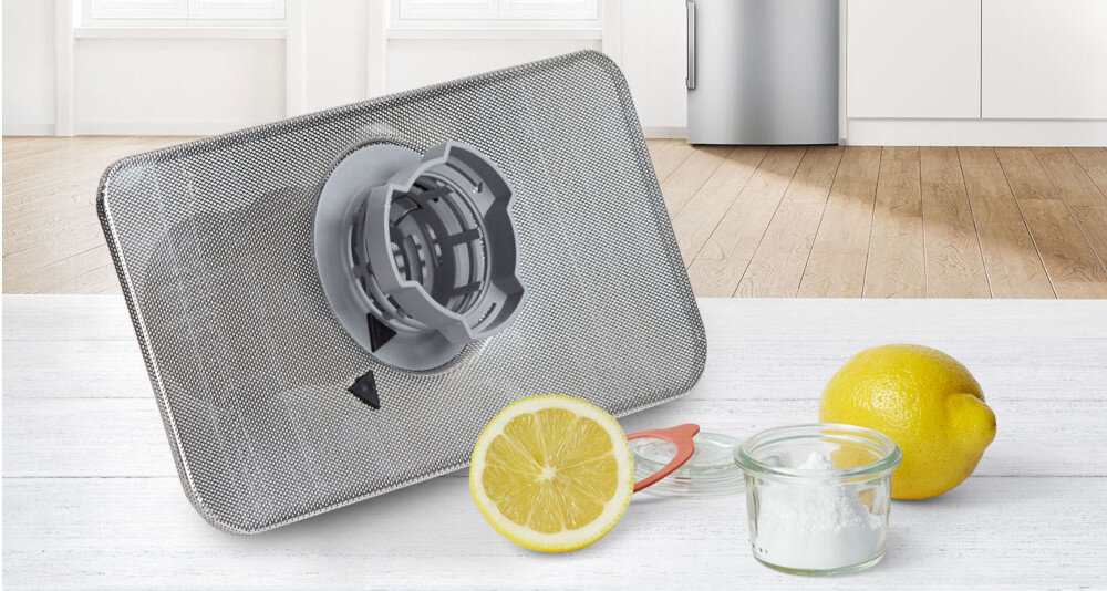 ZMYWARKA BOSCH SMS4HVI14E Na zdjęciu znajduje się stalowy filtr, prawdopodobnie do zmywarki, leżący na blacie w kuchni. Obok filtra umieszczono połówkę cytryny, całą cytrynę oraz mały słoiczek z białym proszkiem (najpewniej sodą oczyszczoną), co może sugerować ekologiczne sposoby czyszczenia lub odświeżania filtrów. W tle widoczna jest lodówka oraz jasne, minimalistyczne wnętrze MachineCare program usuwanie osadów cykl zmywania bez załadunku wysoka temperatura detergenty odkamienianie czyszczenie zmywarka przyjemny zapach długotrwałe działanie lśniący połysk naczyń