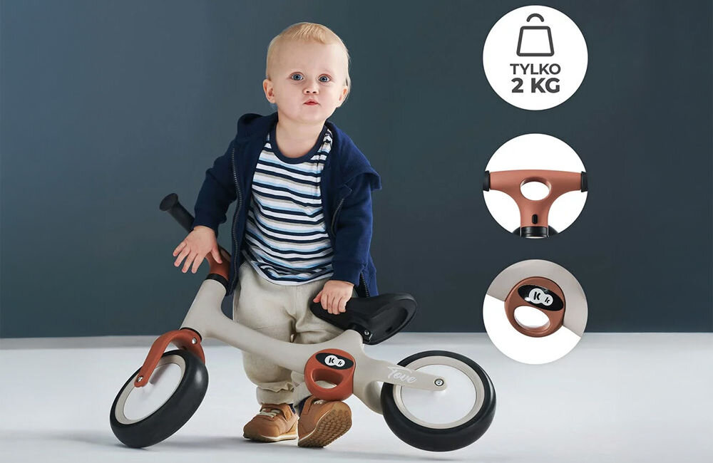 Rowerek biegowy KINDERKRAFT Tove Beżowy dziecko trzyma beżowy rowerek obok pokazane uchwyty ciemne tło wygoda rodziców dwa ergonomiczne uchwyty chwycenie za uchwyty komfortowe niesienie pojazdu ułatwia przemieszczanie się bez zbędnych utrudnień wygodny dla dzieci funkcjonalny dla ich opiekunów 