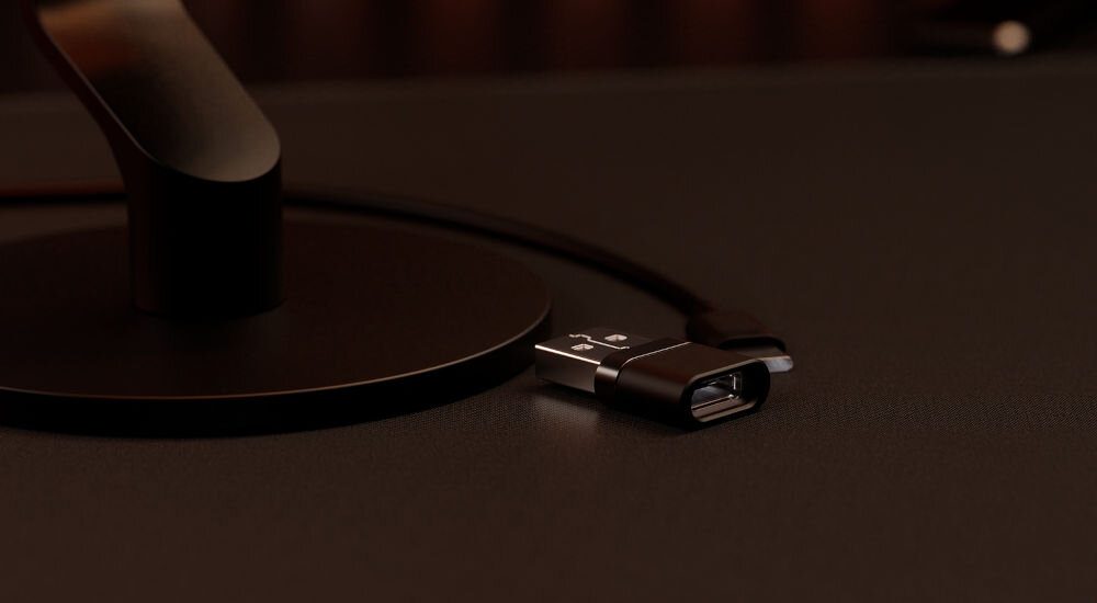 Mikrofon KRUX Pin KRXC018 Kardioidalny Czarny Zbliżenie na mały adapter USB-A leżący na ciemnym biurku obok podstawy mikrofonu, z widocznym fragmentem kabla plug & play port USB-C stabilne cyfrowe połączenie czysty dźwięk komputer urządzenia mobilne konsola PS4 PS5