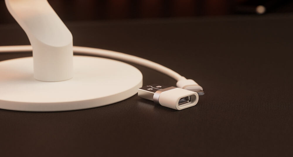 Mikrofon KRUX Pin KRXC019 Kardioidalny Biały Zbliżenie na mały adapter USB-A leżący na ciemnym biurku obok podstawy mikrofonu, z widocznym fragmentem kabla plug & play port USB-C stabilne cyfrowe połączenie czysty dźwięk komputer urządzenia mobilne konsola PS4 PS5