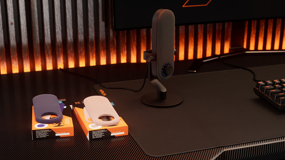 Nakładka na mikrofon KRUX Pin KRXC023 Niebieski Stanowisko gamingowe z mikrofonem KRUX Pin na biurku, na pierwszym planie widoczne opakowania z wymiennymi osłonami w kolorze niebieskim i różowym