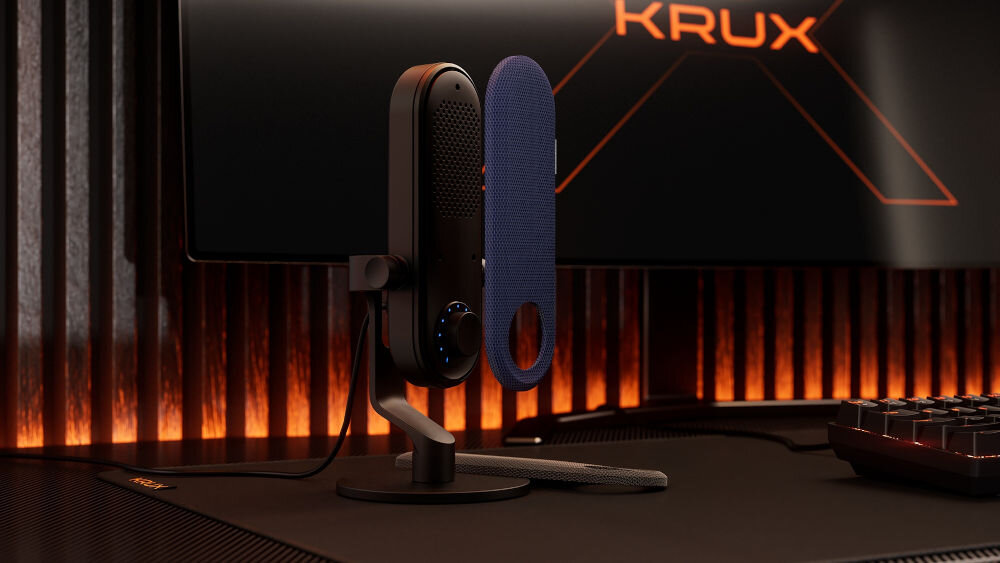 Nakładka na mikrofon KRUX Pin KRXC023 Niebieski Czarny mikrofon KRUX Pin na biurku gamingowym, obok unosi się wymienna niebieska osłona, w tle monitor z logo KRUX i pomarańczowym podświetleniem nadaj charakter wizualna zmiana mikrofonu prosty montaż magnetyczne mocowanie wytrzymała tkanina