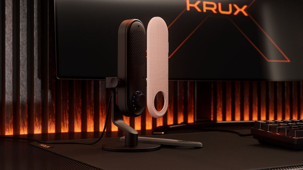 Nakładka na mikrofon KRUX Pin KRXC022 Różowy Czarny mikrofon KRUX Pin na biurku gamingowym, obok unosi się wymienna różowa osłona, w tle monitor z logo KRUX i pomarańczowym podświetleniem nadaj charakter wizualna zmiana mikrofonu prosty montaż magnetyczne mocowanie wytrzymała tkanina