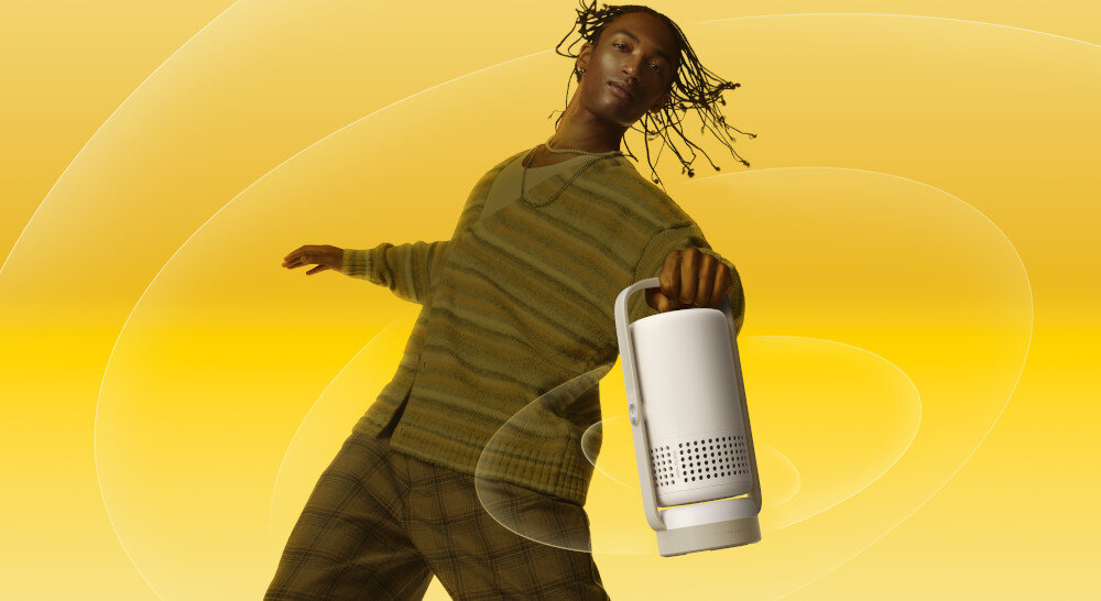 XGIMI Vibe One inteligentny projektor przenośny z wbudowanym akumulatorem lekki poręczny, osoba z projektorem w ręku na żółtym tle