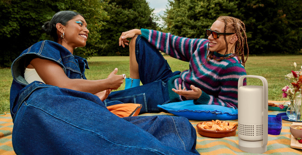 XGIMI Vibe One projektor z oświetleniem ambientowym 8 kolorów sterowanie pilotem, ludzie leżący na kocyku, projektor stojący na kocu