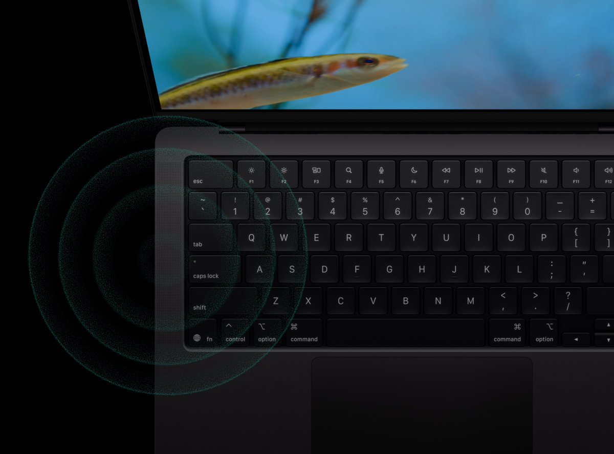 APPLE MacBook Pro Mikrofony o jakości studyjnej system sześciu głośników dźwiękiem przestrzennym Dolby Atmos MacBook Pro spotkań online, pracy z dźwiękiem czy oglądania filmów - Laptop z podświetloną klawiaturą na czarnym tle, ekran z obrazem ryby